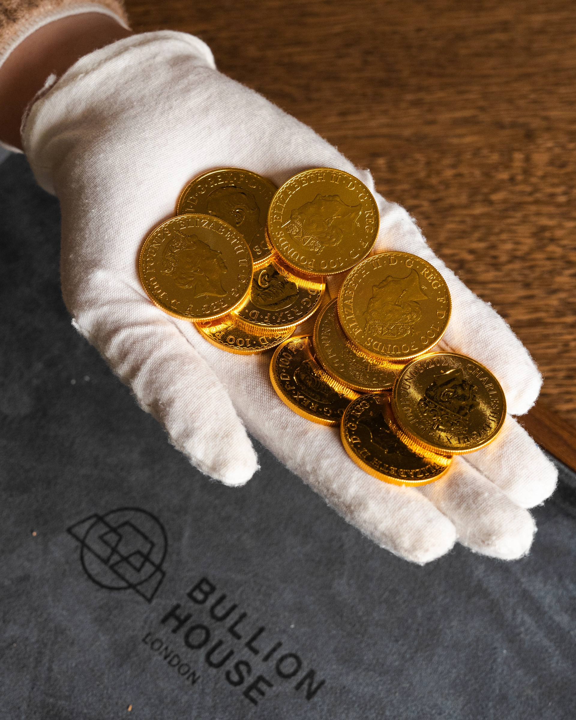 Gold coins held in a white glove above Bullion House packaging