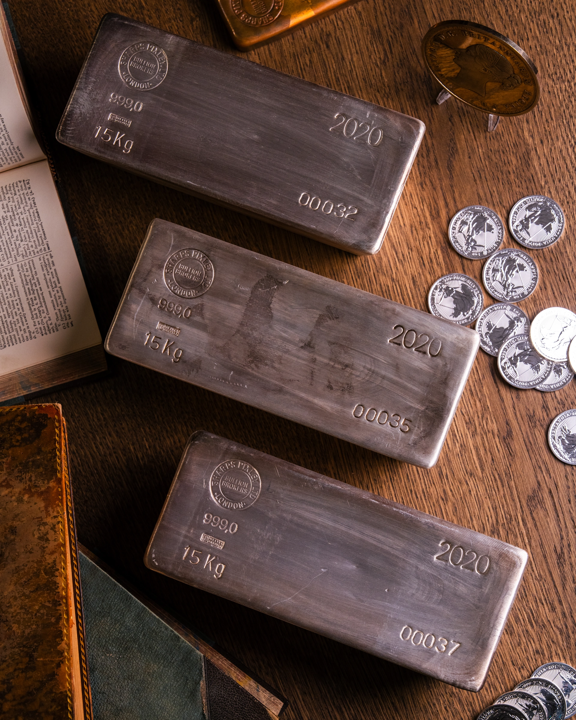Three silver bullion bars with silver coins on a wooden desk