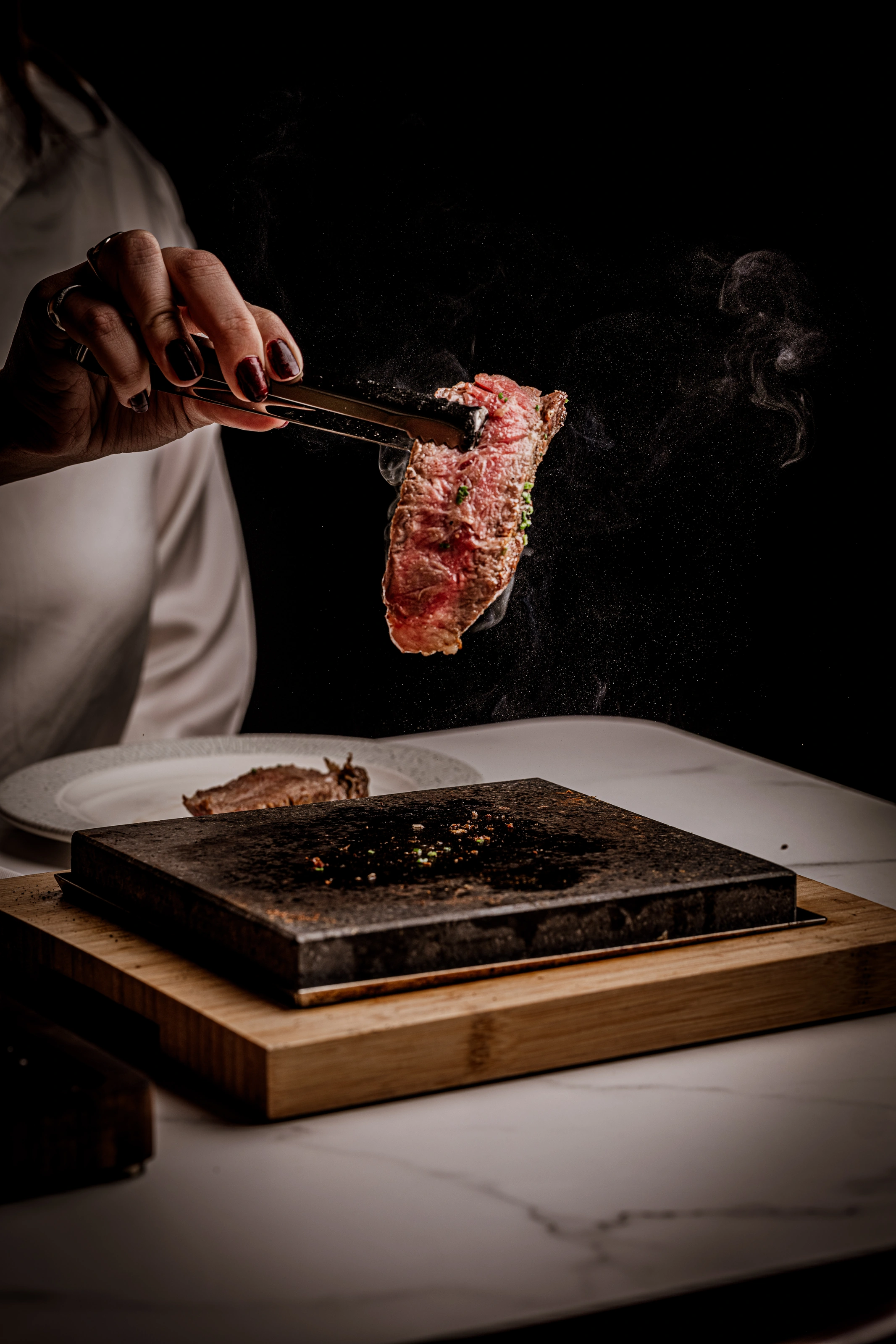 Steak lifted with tongs above a steaming hot stone at Pukush