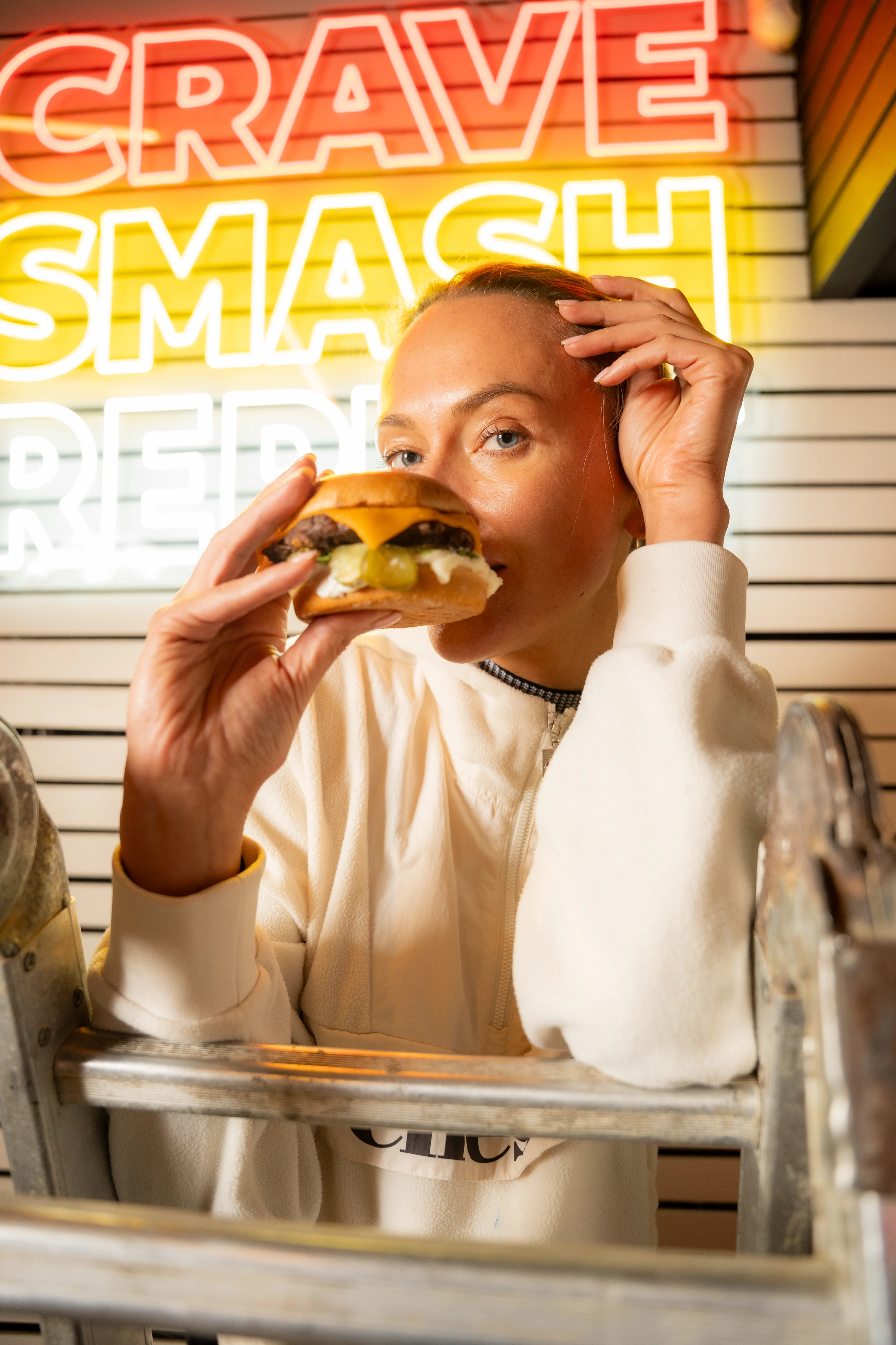 A diner holding a cheeseburger in front of Ranch’s red and yellow neon signs