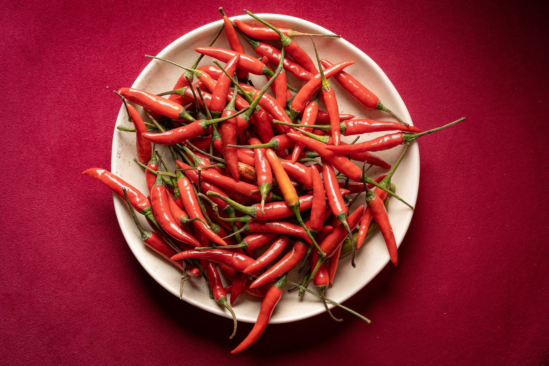 Red and green chillies on a cream plate against a red surface
