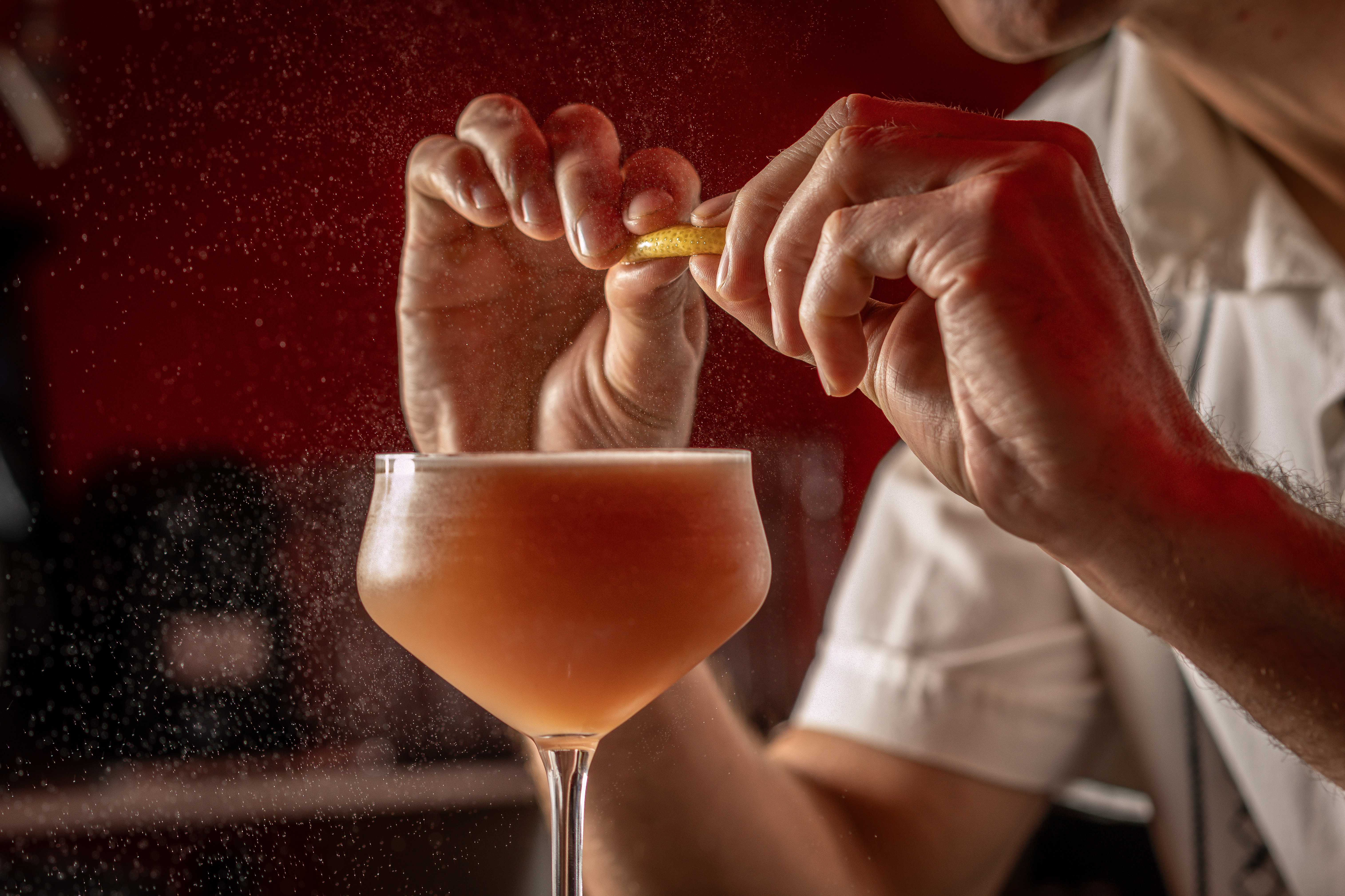 Citrus being squeezed over a cocktail against a red backdrop