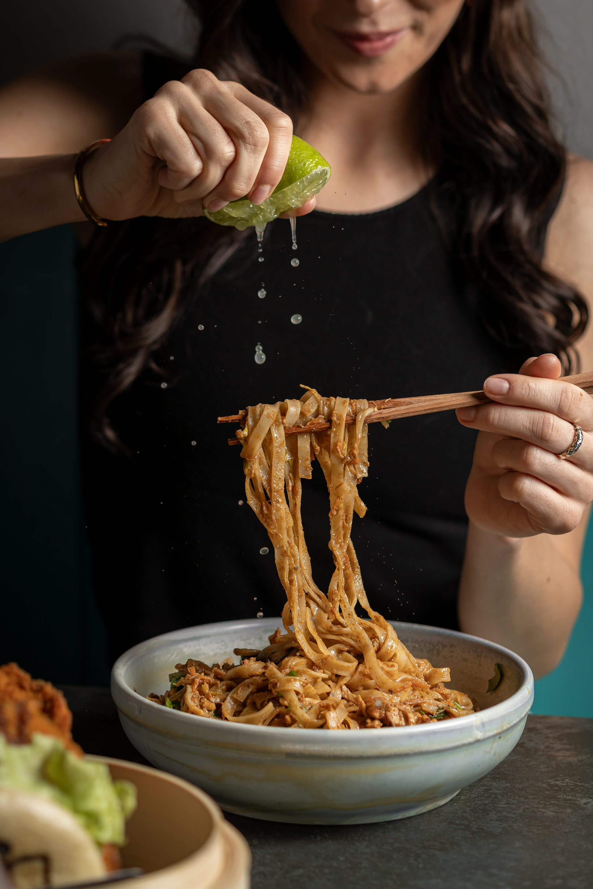 A diner squeezing lime over noodles held with chopsticks