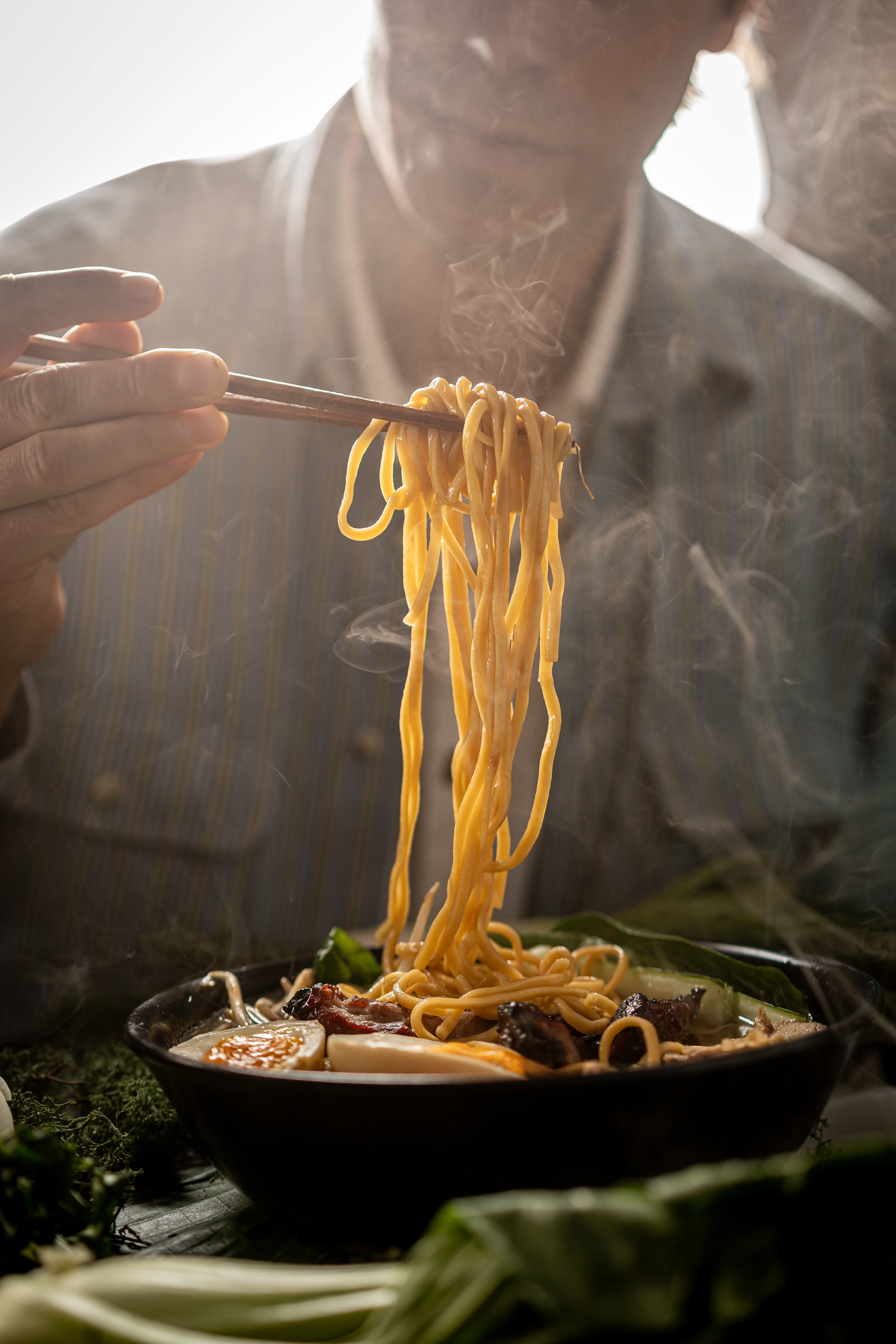 Steaming noodles lifted with chopsticks from a black bowl